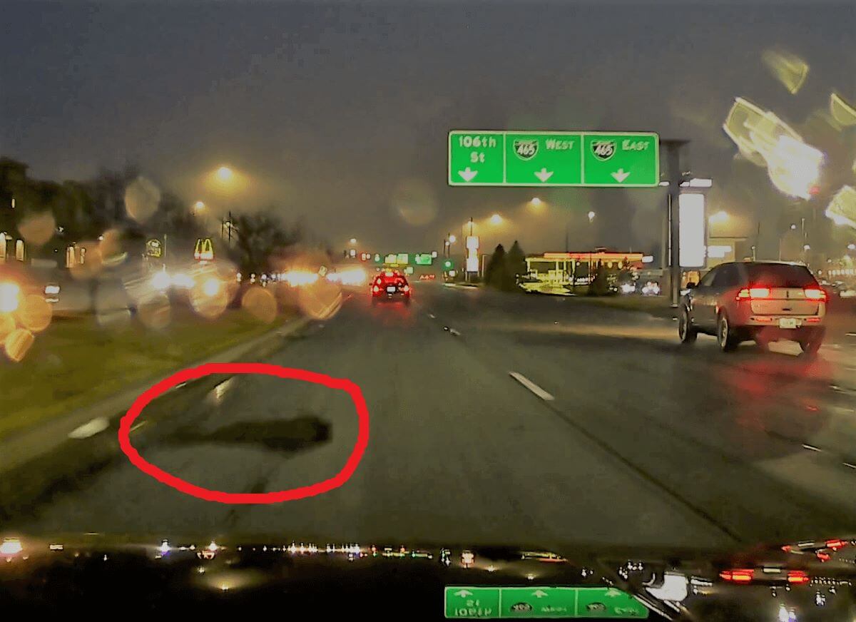 A screen capture from a dashcam showing a large pothole, circled, immediately in front of the capturing vehicle