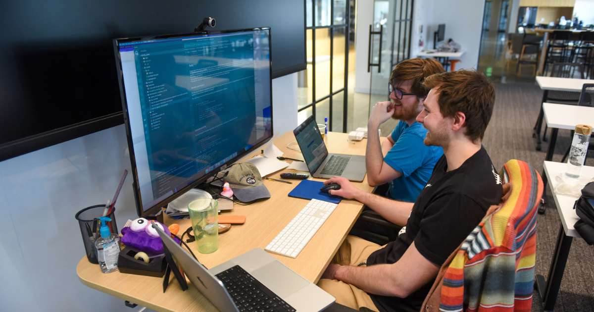 software engineers smiling while working on a large screen with code displaying